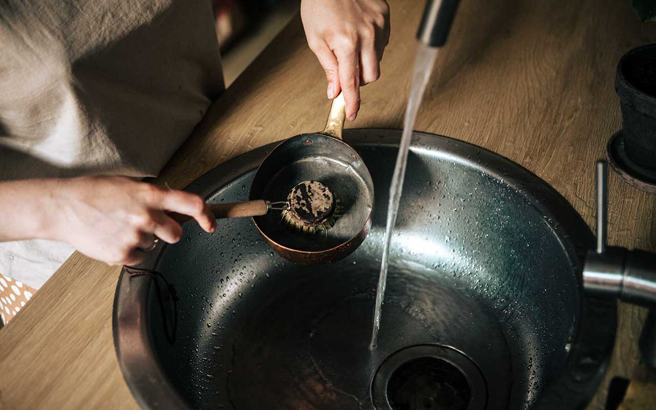 cadru de aproape aratand cum spala vase si toarna ulei in chiuveta conectata de o fosa septica